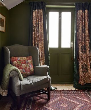 room with dark green walls and woodwork, old wingback armchair, patterned door curtain and antique rug