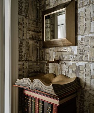 A powder room with book-inspired wallpaper, a book-shaped sink, and a square mirror