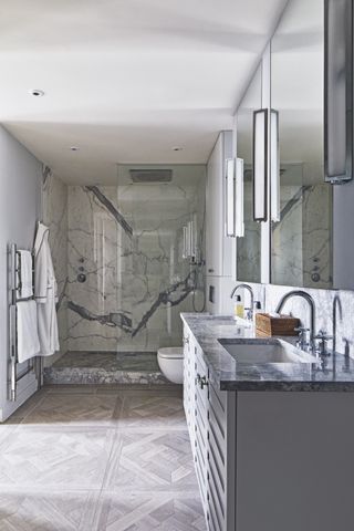 walk in shower with parquet flooring, grey marble countertop on vanity, mirrors, glass shower doors