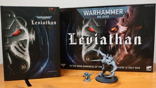 The Warhammer 40,000: Leviathan boxed set with the rule book and two miniatures set out on a wooden table