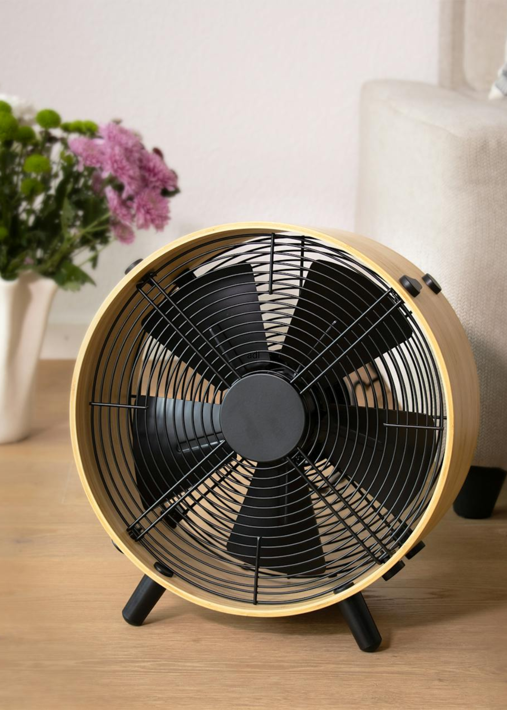 A wood fan with black finishes on a floor beside a sofa and a vase of flowers