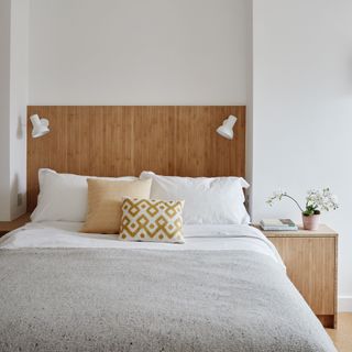 bedroom with timber headboard with built-in bedside lamps and a matching bedside table white and grey bedlinen