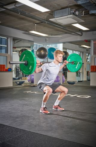 A man in the gym doing a weighted squat with a bar on his shoulders