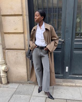 Scandinavian influencer Sylvie Mus wearing a tan trench coat, white button-down shirt, grey jeans, and black slingback heels