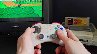 Hand holding Gulikit Elves 2 Pro controller in white to play The Legend of Zelda: A Link to the Past on PAL Super Nintendo and Sony Trinitron CRT TV.