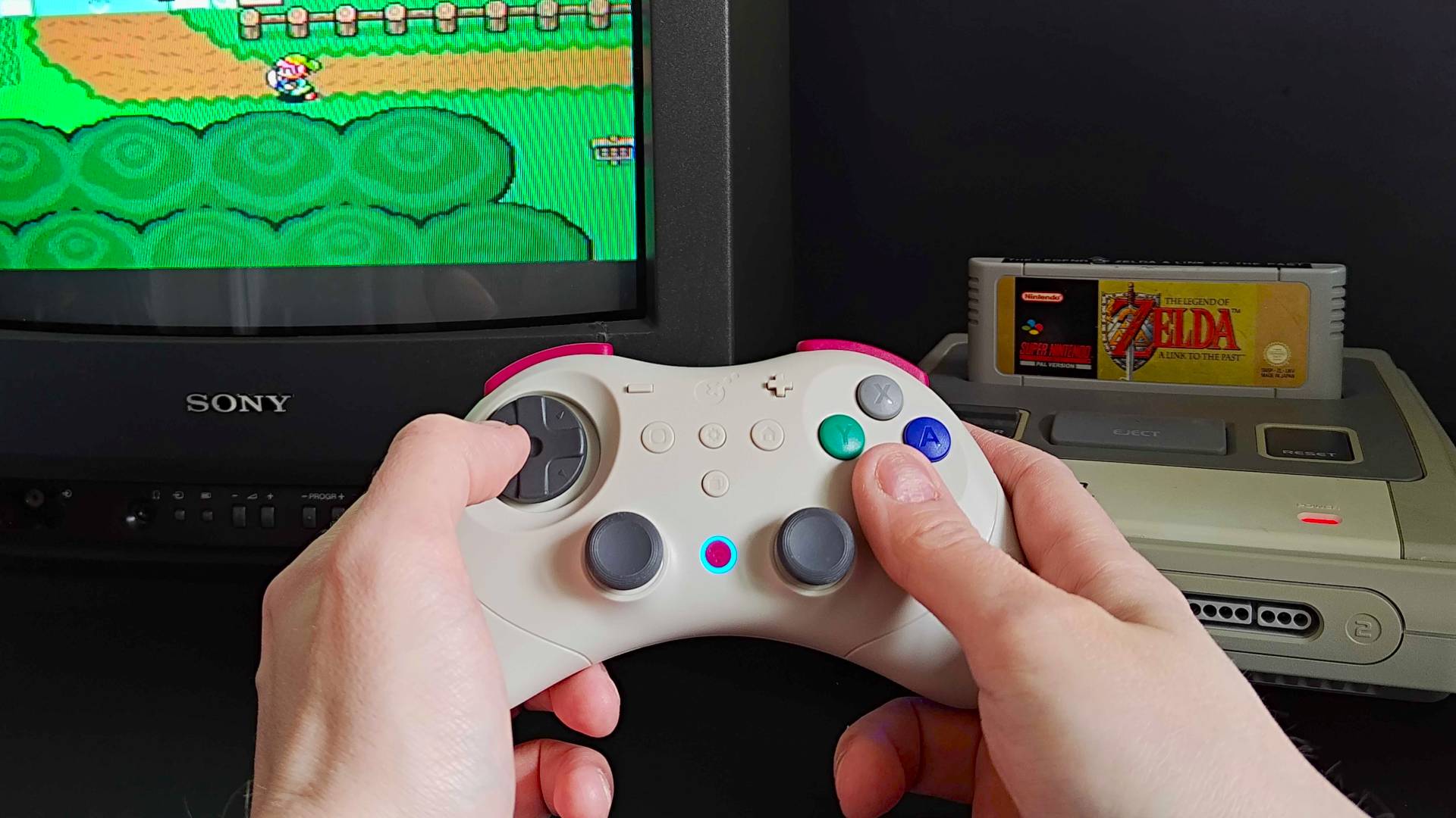 Hand holding Gulikit Elves 2 Pro controller in white to play The Legend of Zelda: A Link to the Past on PAL Super Nintendo and Sony Trinitron CRT TV.