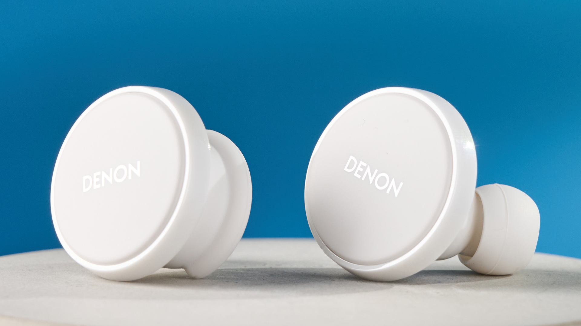 the denon perL Pro wireless earbuds in white, with circular earbud shapes, and a white charging case, photographed against a blue background