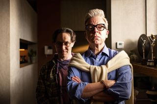 Reece Shearsmith as Simon, standing in half-shadow behind Steve Pemberton as Spencer Maguire at the forefront of the picture with his arms folded, in episode two, 'Simon Says'