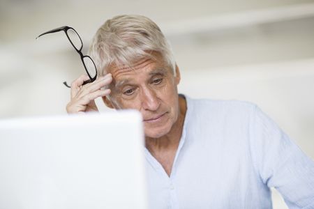 Worried senior man head in hand with laptop on table. He looks concerned but not powerless.