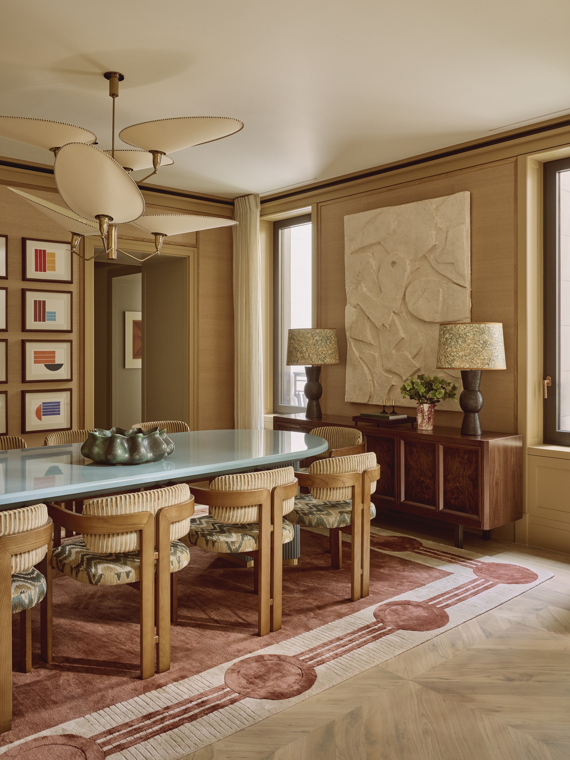 a neutral dining room with a patterned red rug, a light blue lacquer dining table ,and intricate ceiling light