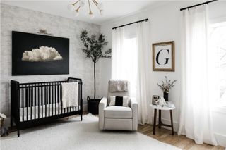 monochromatic boys nursery with hardwood floor, vintage frame, wave wallpaper, white rug, gray armchair, pendant light, side table, black crib and cloud artwork