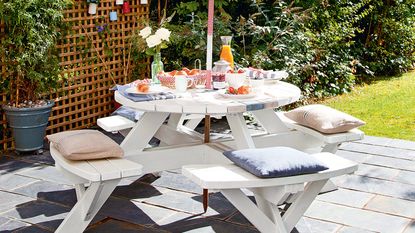 Two deckchairs with colourful cushions on decking by the white wooden clad house with pots of plants