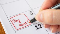 Human hand writing out "pay rent" on calendar