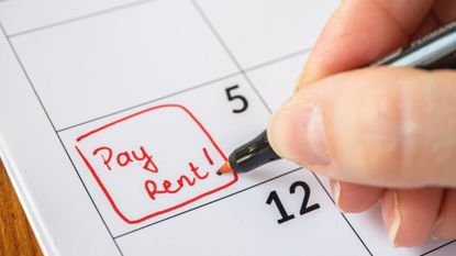 Human hand writing out "pay rent" on calendar