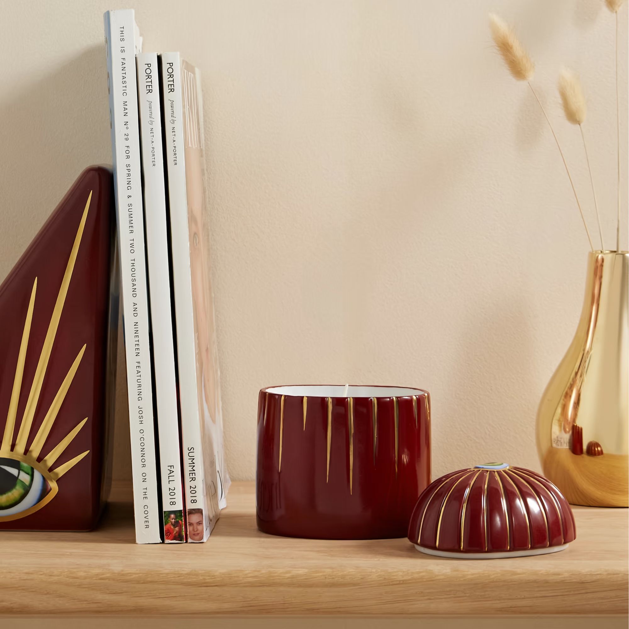 L&#039;OBJET + Lito scented candle on a wooden surface with magazines and dried flowers in a gold vase.