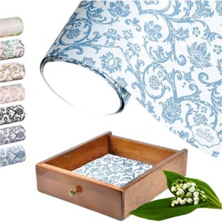 A roll of blue and white patterned drawer liner with a brown lined wooden drawer below