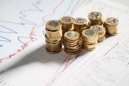Stack of pound coins on financial graphs and figures. 
