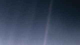 A hazy blue scene of space. In a mote of dust, a tiny speck is actually Earth.