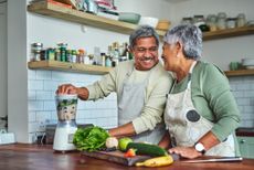 An older, healthy couple preparing a smoothie in their kitchen.