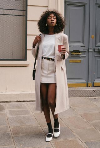 a photo of a woman wearing a classic outfit with a long coat and t-shirt and mini skirt and ballet flats