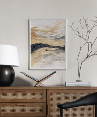 A gold and black artwork above a console table with decor on it