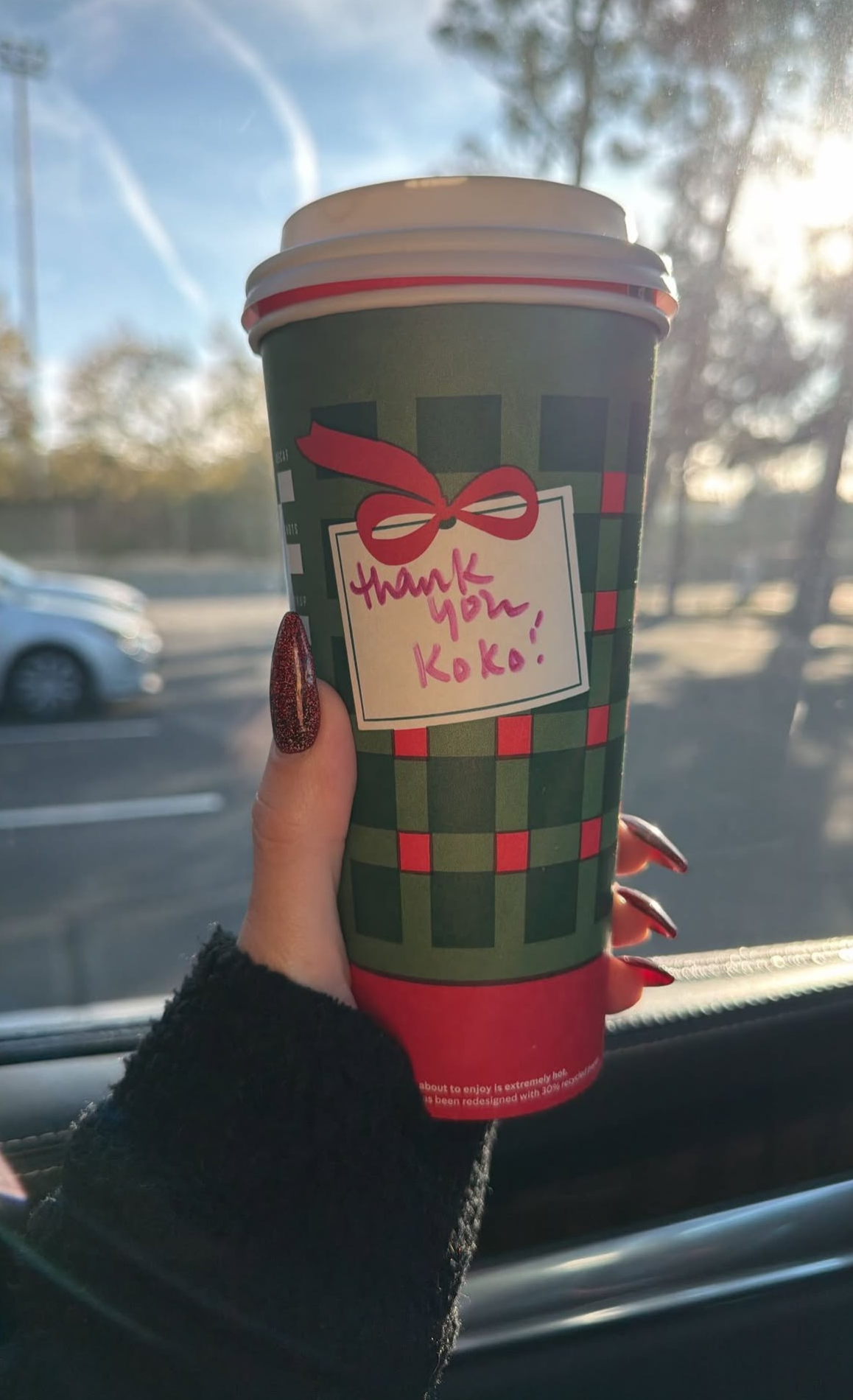 a photo of a person with red nails holding a holiday-themed coffee cup