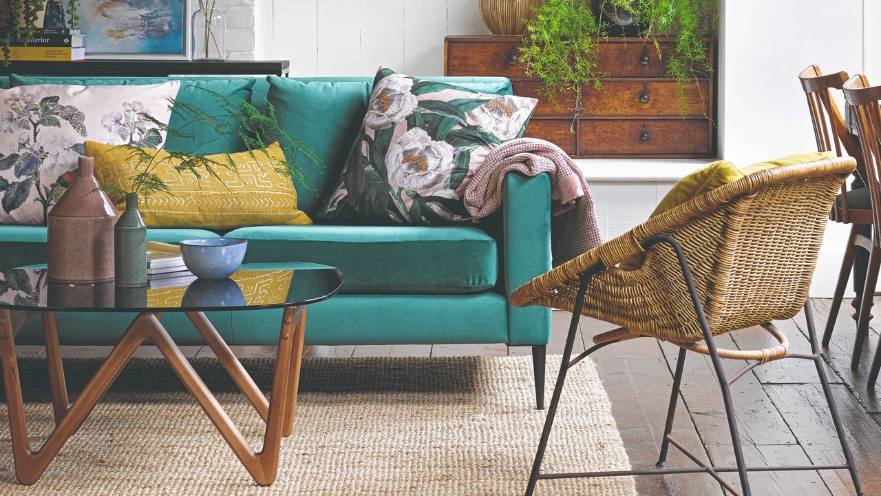 A living room with a green velvet sofa and floral cushions on a jute rug with a round glass coffee table