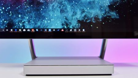 A sleek computer monitor with a galaxy-themed wallpaper and visible taskbar icons is set against a gradient pink and purple background, conveying a futuristic vibe.