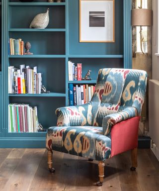 Blue painted book storage in the corner of a room with decorative armchair with pink sides