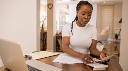 A young woman does financial paperwork at her dining room table.