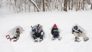 Four snowshoers sit in holes in deep snow in Mill Creek Canyon Utah