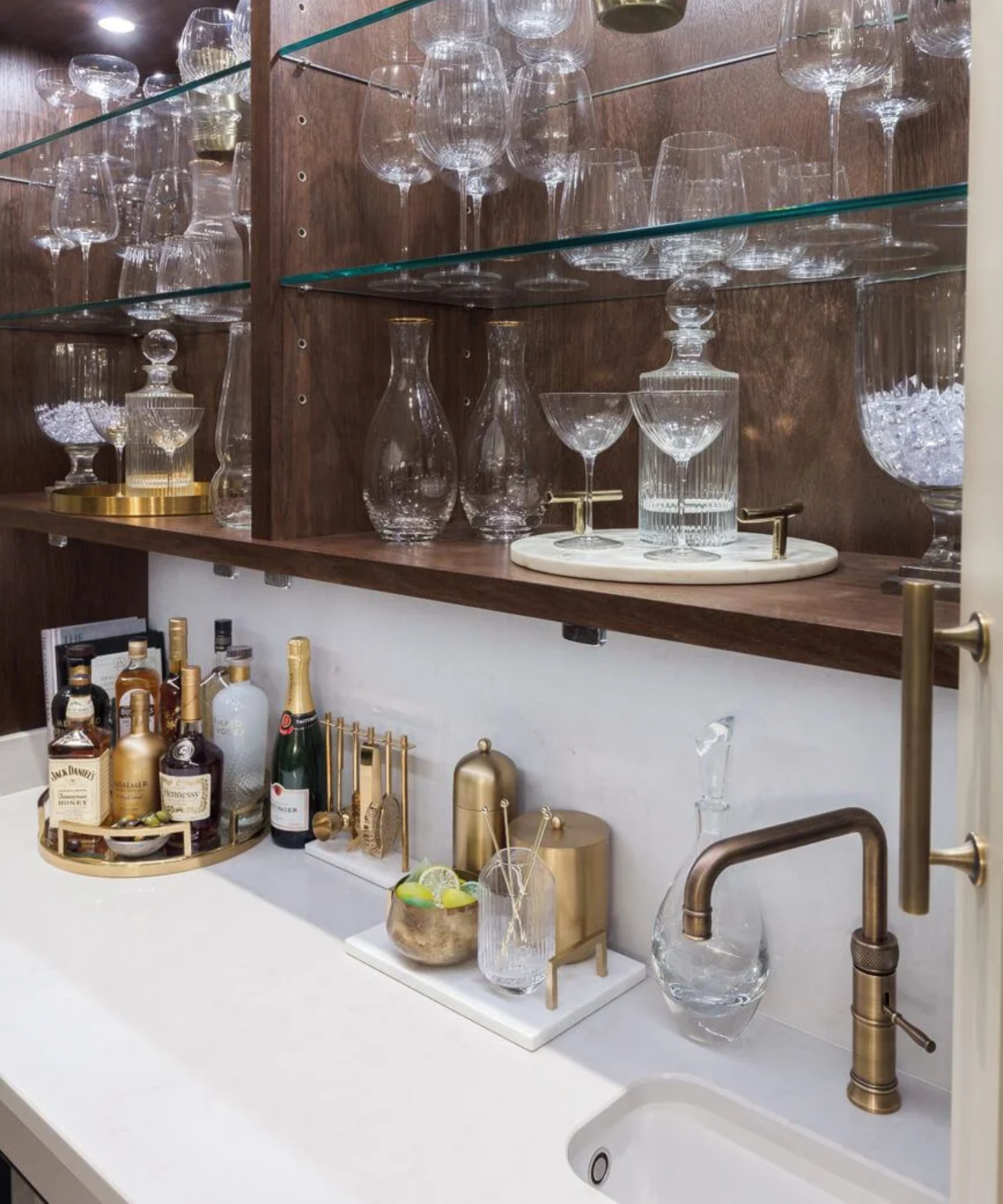 Home bar with sink, white worktop and shelves filled with glasses and decanters