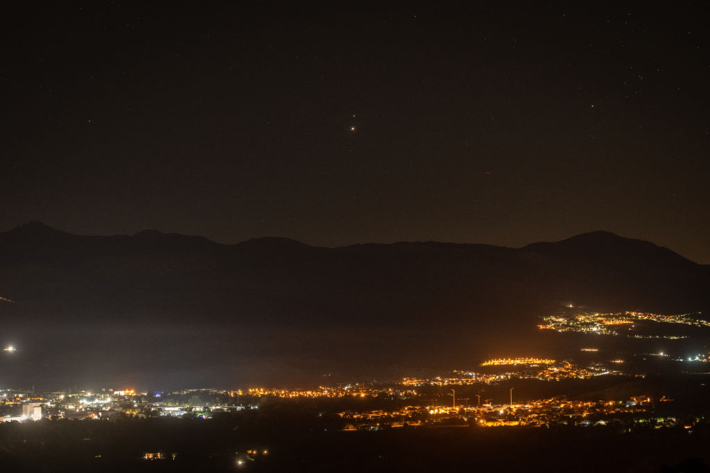 city lights shine brightly below but two bright 'lights' in the sky are visible, one brighter - jupiter and one dimmer - mars.