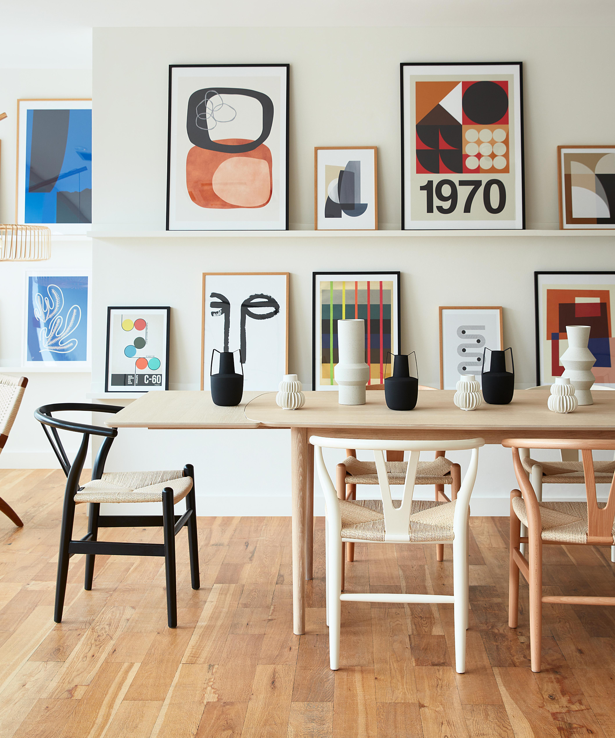 dining room with pictures shelves displaying lots of framed artwork, light wood oval dining table and wooden chairs in different shades