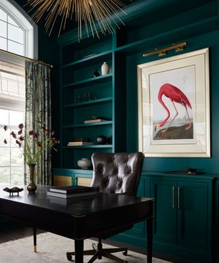 moody home office with dark teal wall and built-ins, black desk and swivel chair