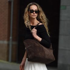 Woman wearing white maxi skirt, black sweater, and large suede tote bag.