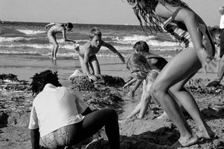 A black and white beach scene depicting children playing and digging in the sand