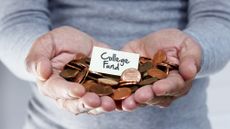 A man holds a handful of pennies with "college fund" written on a small white card on top of the pennies.