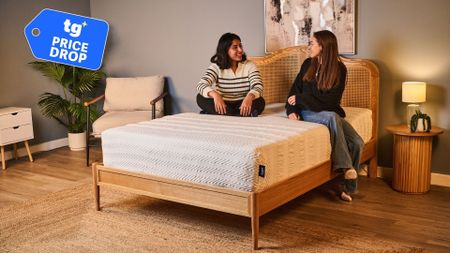 An image showing two women sitting on the Leesa Legend Hybrid Mattress. A Tom's Guide price drop deals badge is in the top left foreground to show that the mattress is 30% off in the Labor Day sale. 