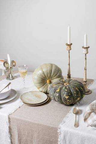 white and natural table setting with earthenware plates, vintage cutlery and candlesticks, two green pumpkins