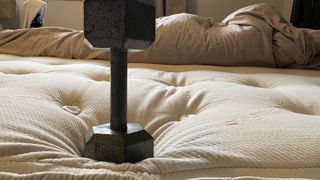 Our reviewer places a black weight on the edge of the Naturepedic Concerto mattress to test edge support