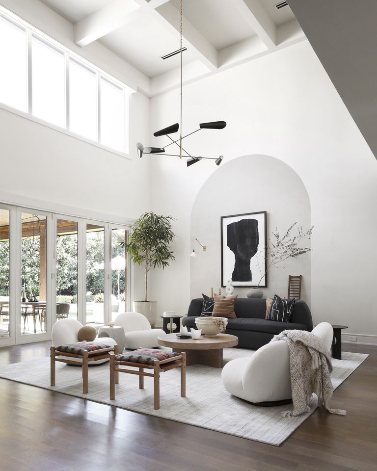 white living room with vaulted ceiling, monochromatic scheme, wooden floors, outdoor space through doors, modern furniture, black pendant light 