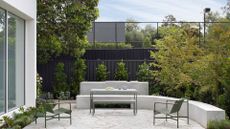 A backyard with metal green outdoor furniture, tall trees and a black fence