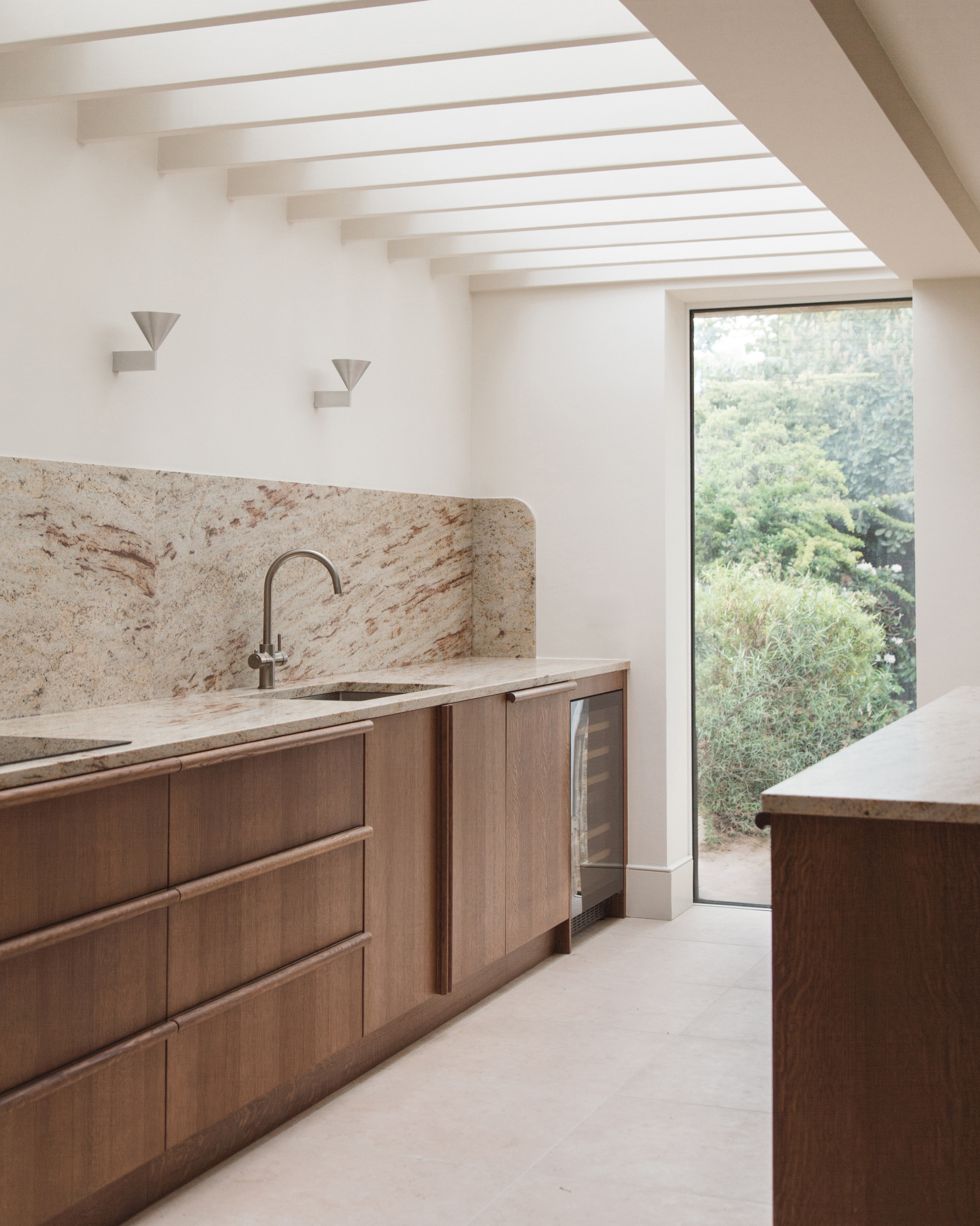 A galley kitchen with wooden cabinetry, stone counters and white walls