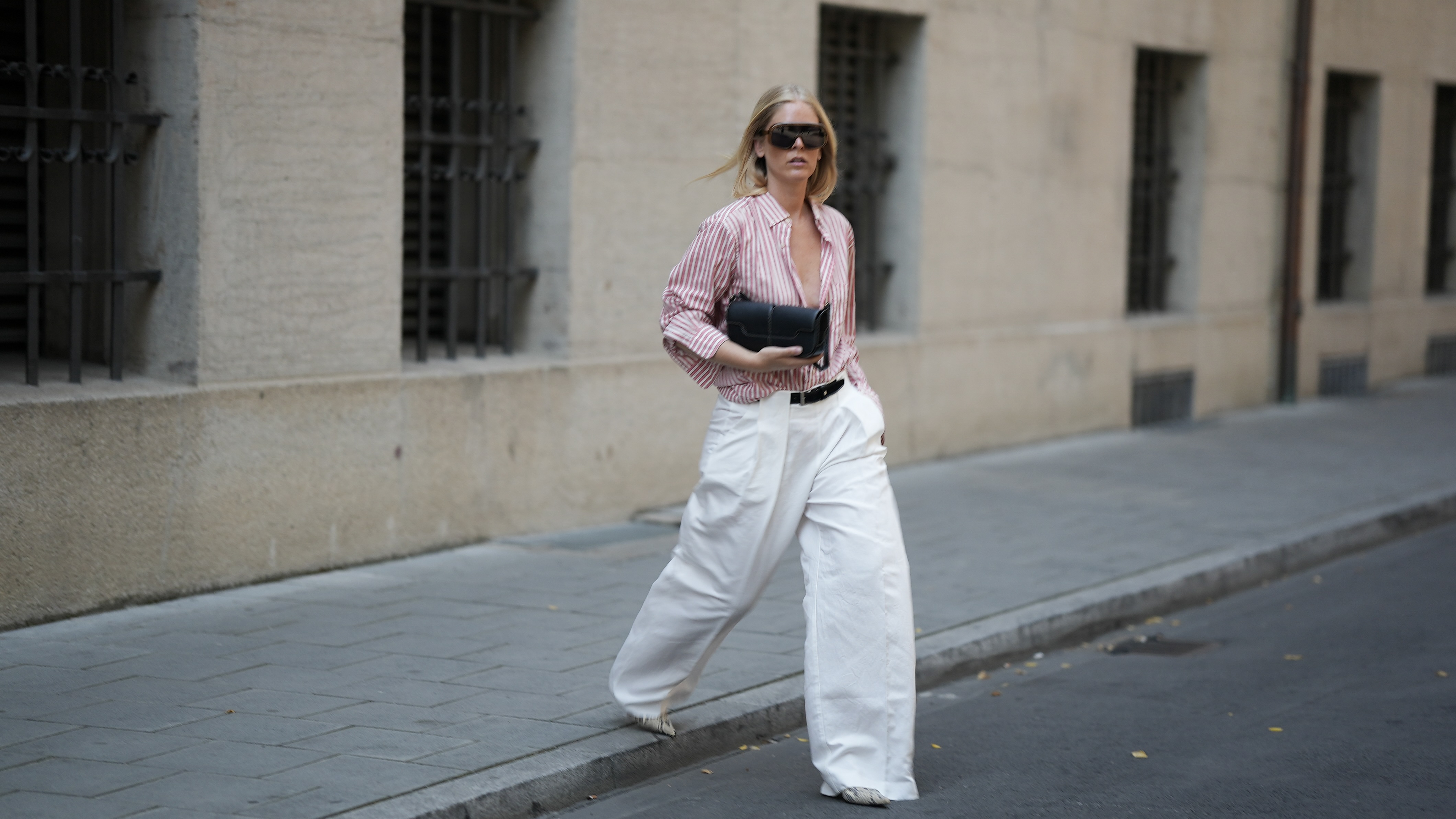 Stylish woman crossing the street wearing a red and white striped button down and oversized white pants holding a black clutch