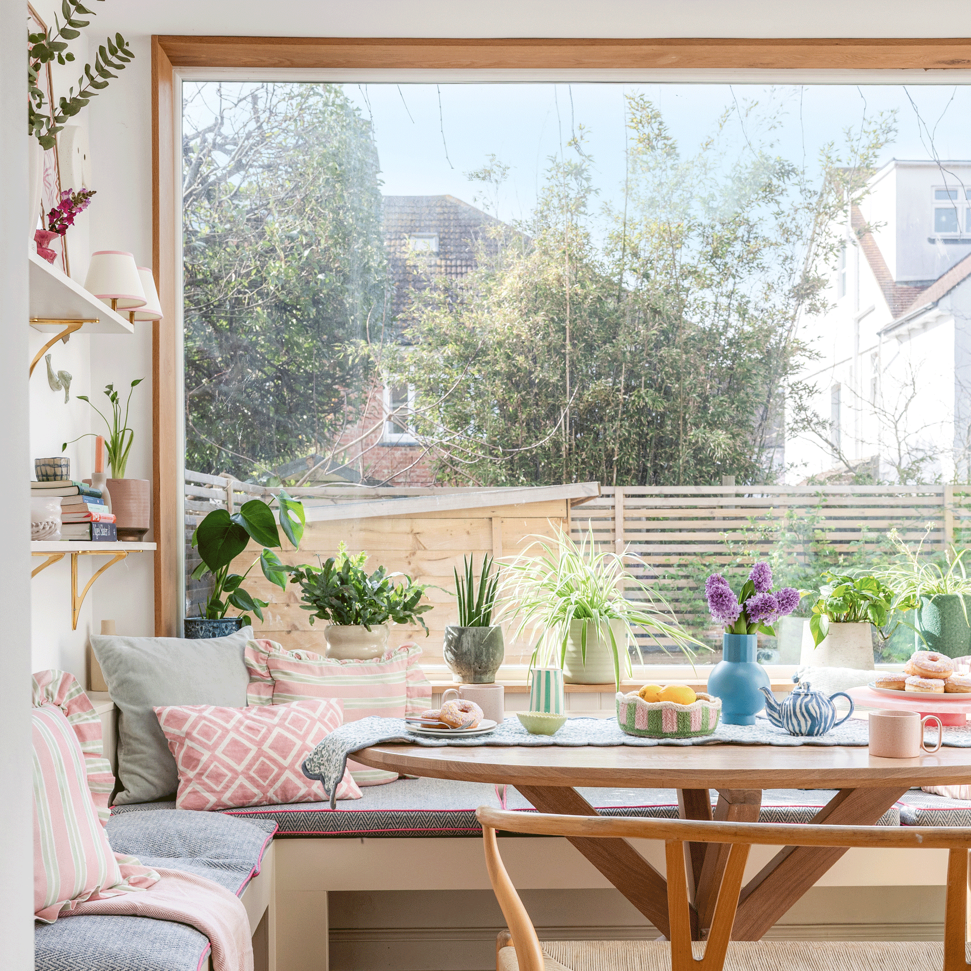 an open plan kitchen diner with banquette seating and a wishbone bench, open shelving and a large picture window facing the garden