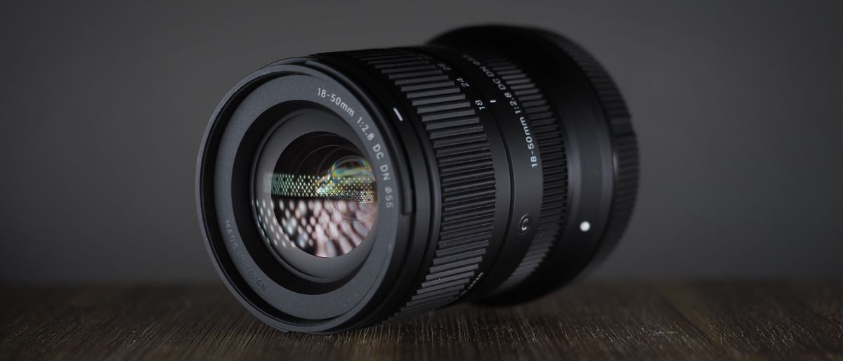 Sigma 18-50mm f/2.8 DC DN | C in Canon RF mount, on a wooden surface against a dark background, moodily lit