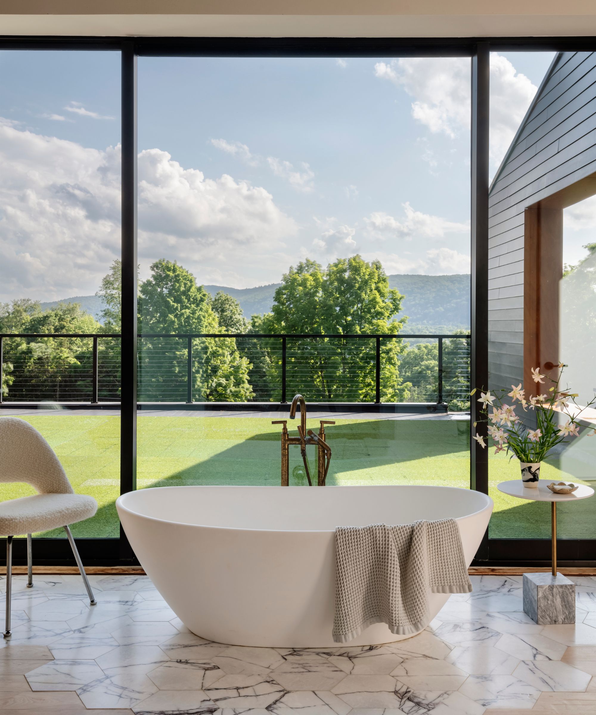 A freestanding tub in a bedroom styled with a boucle chair and a side table topped with fresh flowers