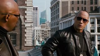 Dwayne Johnson, wearing cool sunglasses and a leather jacket, smiles to his NYPD partner in The Other Guys