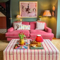Green living room with pink sofa, pink painting with horse and pink and white striped fabric ottoman acting as coffee table